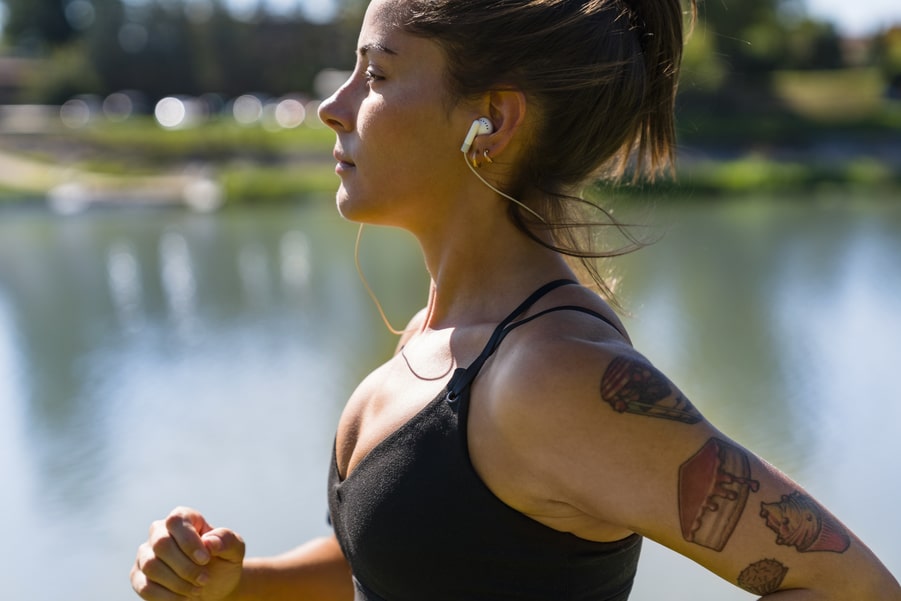 Tattooed young woman with earbuds jogging at the riverside.